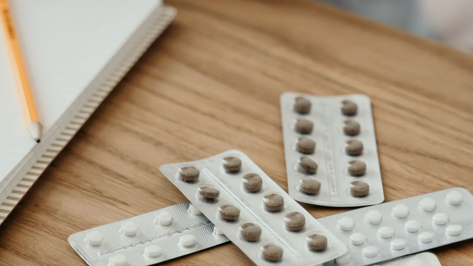 Cartelas de medicamento e um caderno aberto sobre uma mesa de madeira